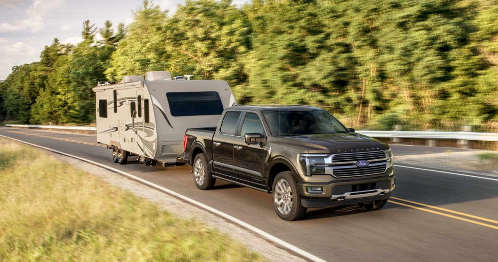 A Ford truck driving on a scenic road hauling a camper